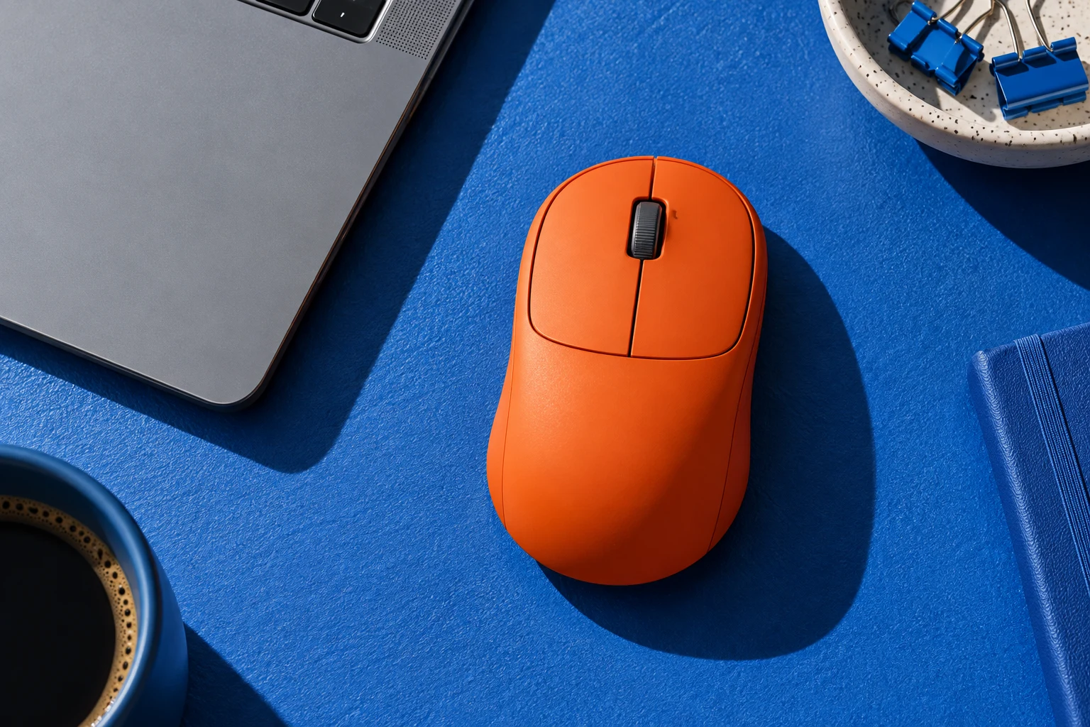 Illustration of an orange wireless mouse on a cobalt-blue desktop beside a laptop