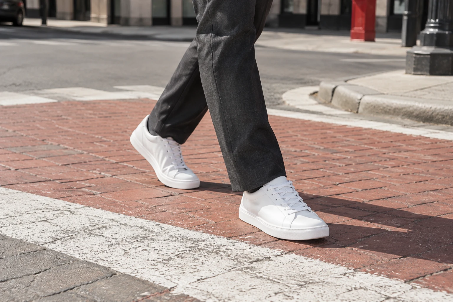 Illustration of a person wearing white sneakers and charcoal trousers on a brick crosswalk